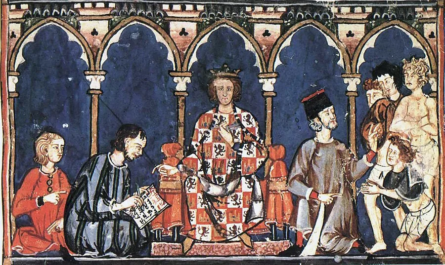 A medieval manuscript miniature of a crowned King Alfonso X of Castile, seated under a Gothic arcade in a red-and-gold castle-and-lion robe, with a scribe writing at his feet and courtiers gathered beside him.