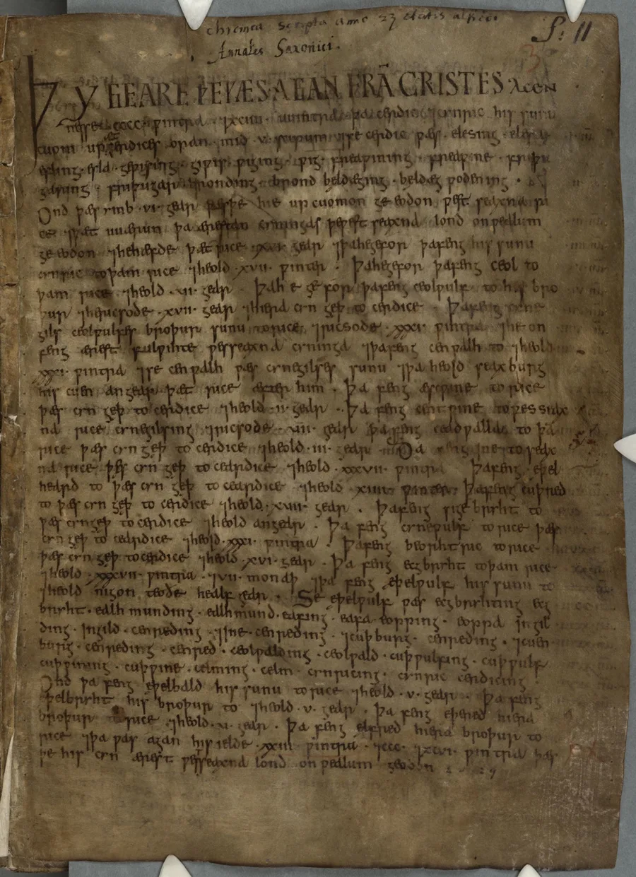 A browned parchment page of the Parker Chronicle written in dense Old English minuscule, opening with the enlarged darker line 'ÞY GEARE...' beneath later annotations in the top margin; small marginal notes run down the right edge.