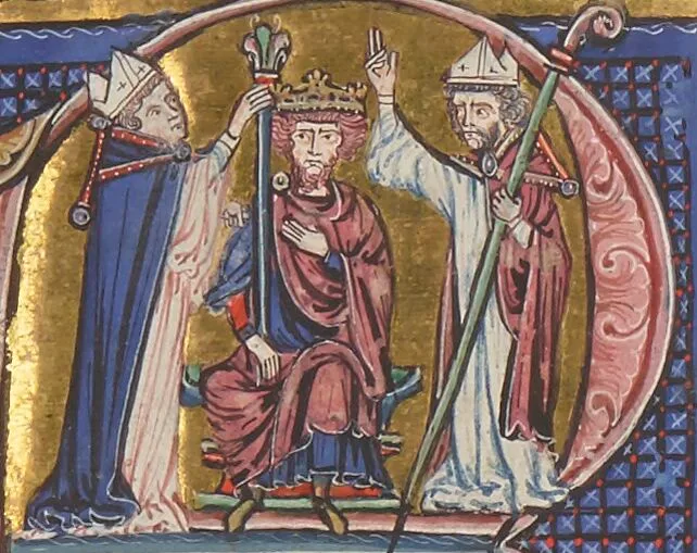 A gold-ground manuscript miniature: a crowned, seated king in red robes is crowned by two bishops in blue and white vestments holding croziers, framed inside an ornate blue capital letter.