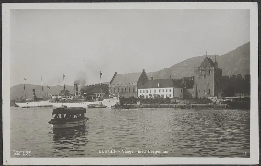 Black-and-white 1920s postcard photograph of Bergen's Vågen harbour, a steamship and small boats on the water before the Bergenhus fortress complex, Håkonshallen and the Rosenkrantz Tower along the waterfront.