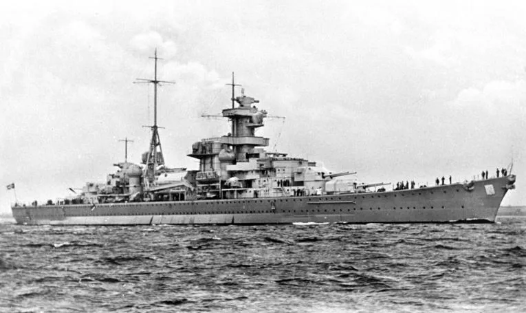Black-and-white 1939 photograph of the German heavy cruiser Blücher underway at sea, viewed from the starboard side, sailors visible on deck against open water.