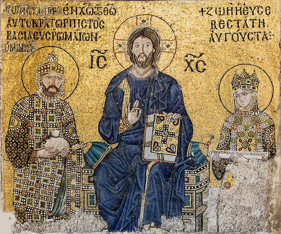 Gold-ground mosaic in Hagia Sophia: Christ Pantocrator enthroned at center holding a jeweled Gospel book, flanked by a crowned, bearded emperor in patterned imperial dress at left and a crowned empress in matching jeweled robes at right, Greek inscriptions in the gold background.