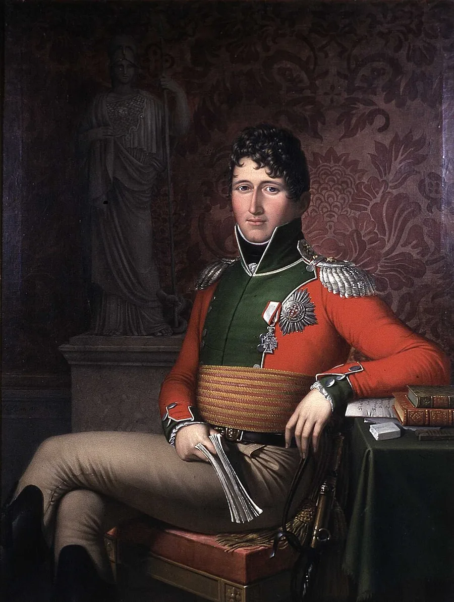 Painted portrait of a young, dark-curly-haired man in an elaborate green-and-red military coat with silver epaulettes and a chest medal, seated with papers in hand beside a shadowed classical statue, 1813.
