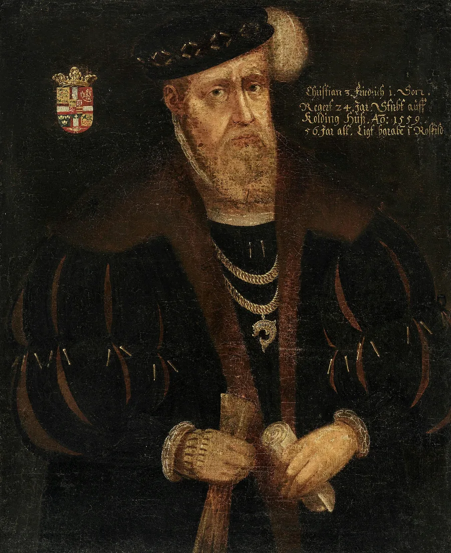 Half-length portrait of an older bearded man, Christian III, in black fur-collared court dress with two gold chains and a badge, a black studded cap, a coat of arms upper left, and a Danish inscription noting his 1559 death at Kolding.