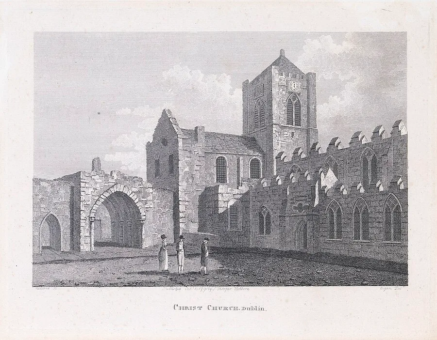 1790s engraving lettered 'Christ Church, Dublin': the cathedral's square battlemented clock tower and long crenellated quire wall in weathered stone, a ruined arch at left, and three figures in eighteenth-century dress on the open ground before it.