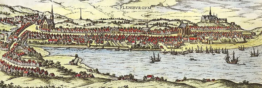 Hand-colored bird's-eye engraving of Flensburg on its fjord, ships riding at anchor in the harbor and the walled town with red-roofed houses and church spires rising behind the quay.