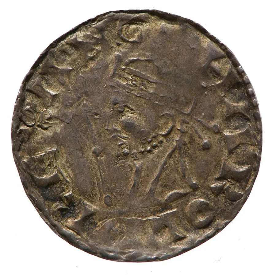 The obverse of a worn silver penny of Harold II: a crowned, bearded bust facing left with a beaded tie at the neck and a scepter rod before the face, ringed by a partly legible legend, photographed against plain white.