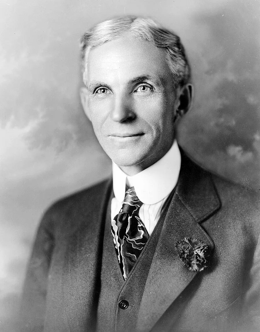 Black-and-white 1919 studio portrait of Henry Ford, gray-haired, in a formal suit with a boutonniere, facing the camera with a faint smile.