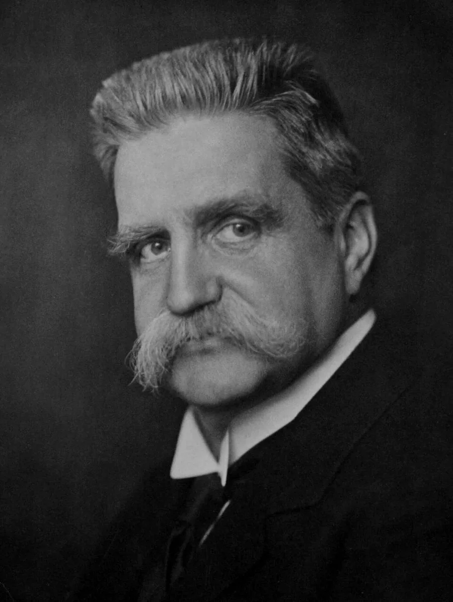 Close studio portrait of a man with swept-back white hair and a large white moustache, no beard, wearing a dark suit with a high wing collar and tie — Hjalmar Branting, 1917.