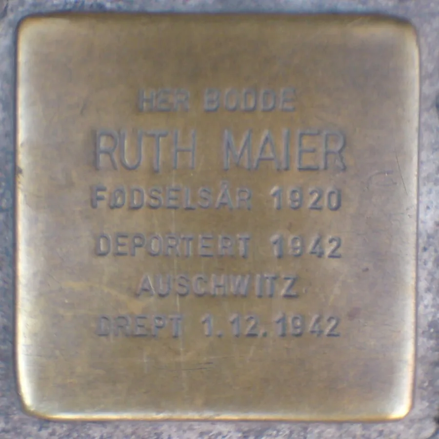 Close photograph of a small square brass Stolperstein memorial stone set flush into a paved street, engraved in Norwegian with a name, birth year, and deportation and death details.
