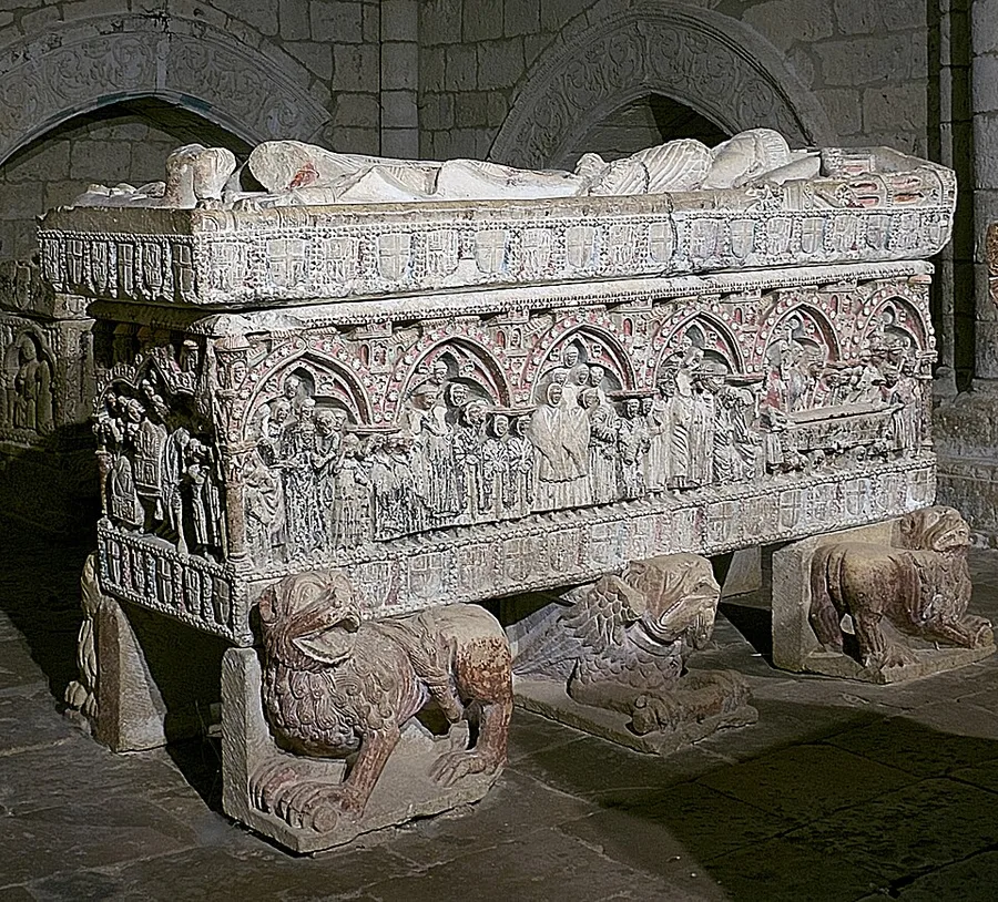 A Gothic stone tomb resting on carved lion figures, its lid bearing recumbent effigies and its sides carved with a procession of mourning courtiers — the tomb of Infante Felipe of Castile at Villalcázar de Sirga.
