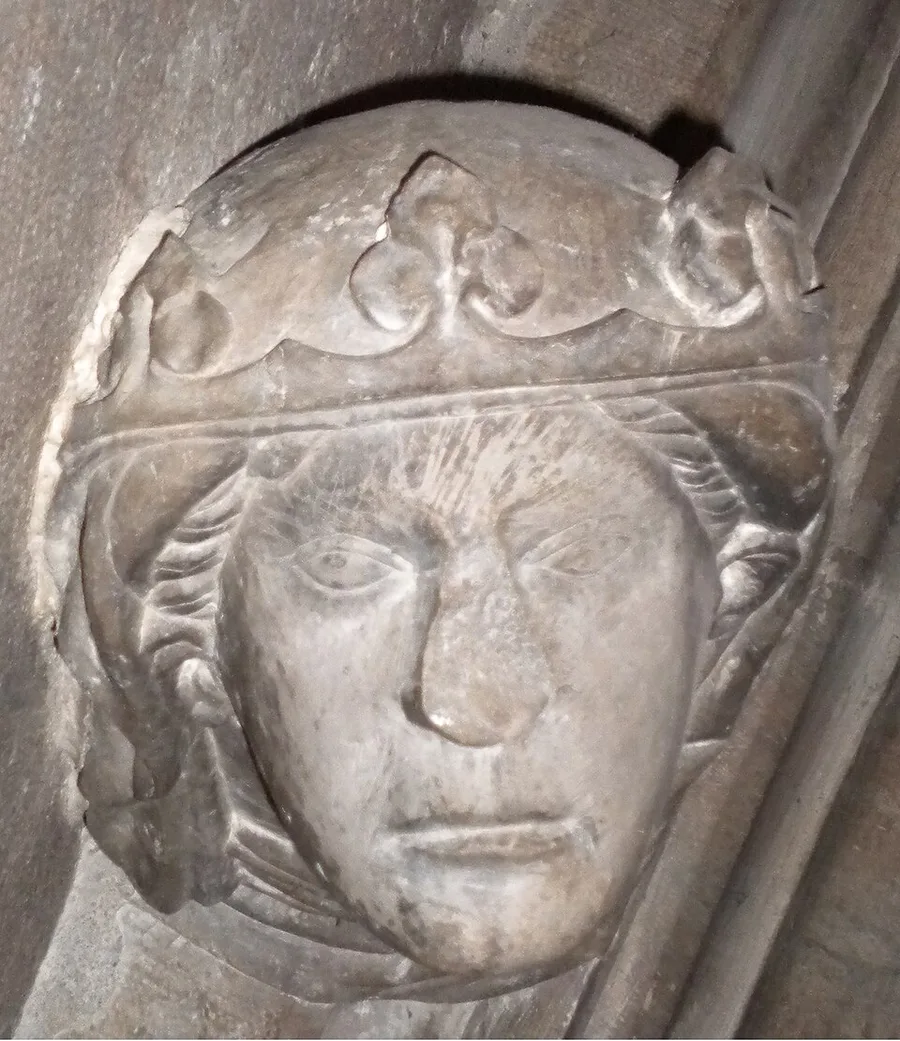 Close-up of a weathered stone corbel bust of a woman wearing a fleur-de-lis crown, carved into a cathedral wall corner and identified as Duchess Ingeborg of Norway.