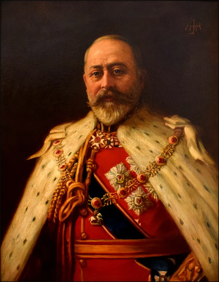 Painted portrait of an elderly bearded man in ermine-trimmed ceremonial robes over a red sash, with the star and collar of a chivalric order across his chest — King Edward VII, 1903.