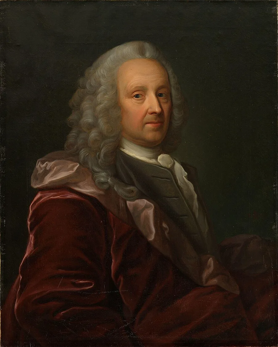 Half-length oil portrait of a bewigged 18th-century man in a dark red velvet coat over a grey waistcoat and white cravat, turned slightly to one side against a dark ground.