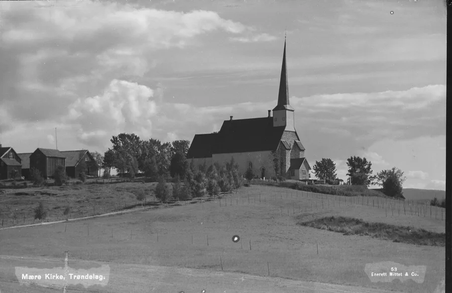 Early-20th-century Mittet & Co. photograph: Mære Church, with its tall slender spire, stands on its knoll above open fields under a clouded sky, farm buildings and trees at left and a fenced lane curving up the rise; caption 'Mære Kirke, Trøndelag' at lower left.