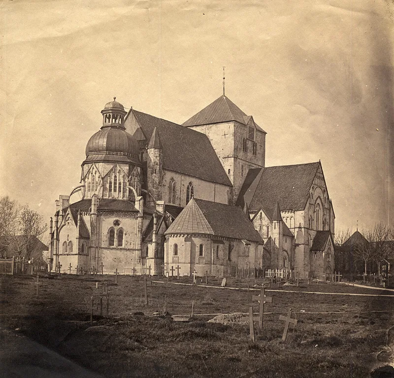 One of the earliest surviving photographs of Norway (1857): Nidaros Cathedral seen from the northeast in sepia tone, weathered medieval stonework before its later restoration, with a churchyard of wooden crosses in the foreground.