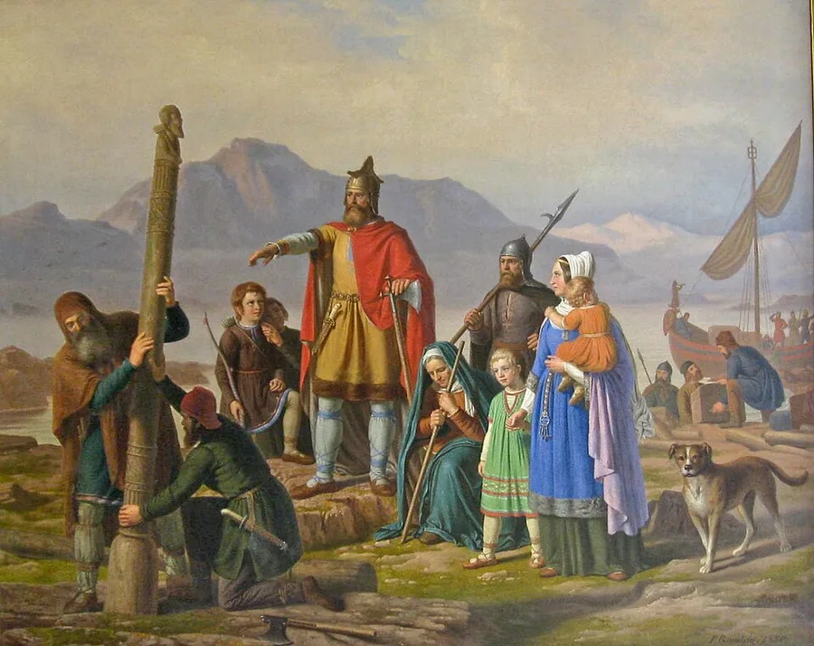 A 19th-century oil painting: two men raise a tall wooden pillar carved with a face at its top on a rocky shore, while a helmeted, red-cloaked chieftain gestures outward; a family with children and a dog stand nearby as men unload a ship in the background beneath mountains.