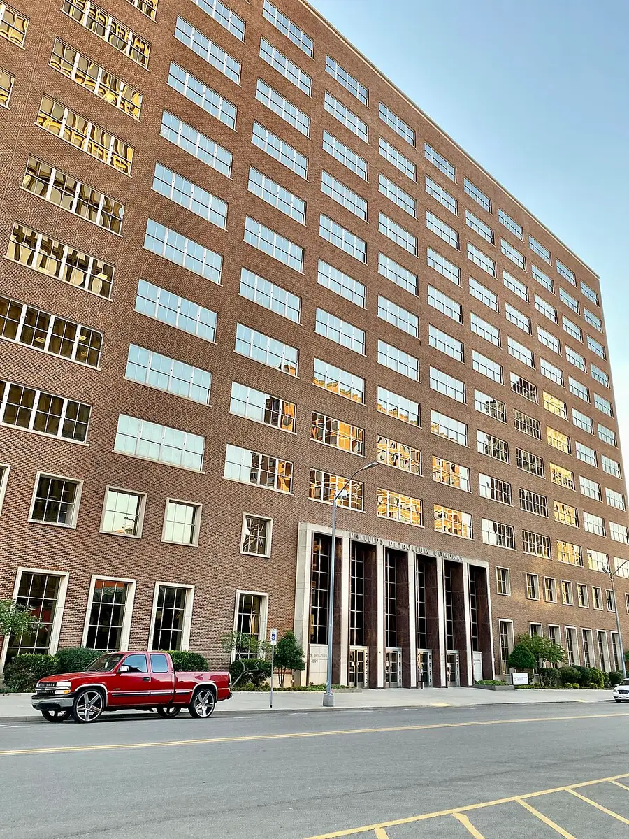 The brick Adams Building in Bartlesville, Oklahoma, rising more than ten stories over a street with a red pickup truck at the curb, 'Phillips Petroleum Company' carved above its colonnaded limestone entrance.