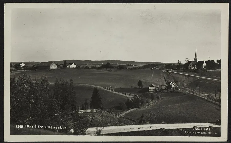 A 1924 photograph of the Romerike farmland at Ullensaker — rolling fields, farm buildings, and a white church spire under the wide eastern-Norway sky.