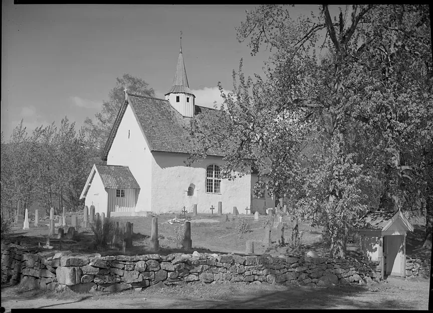 A late-1930s photograph of the whitewashed medieval stone church at Seljord, its churchyard gravestones and dry-stone wall in front — the church where legend hangs seven invisible huldra tails.