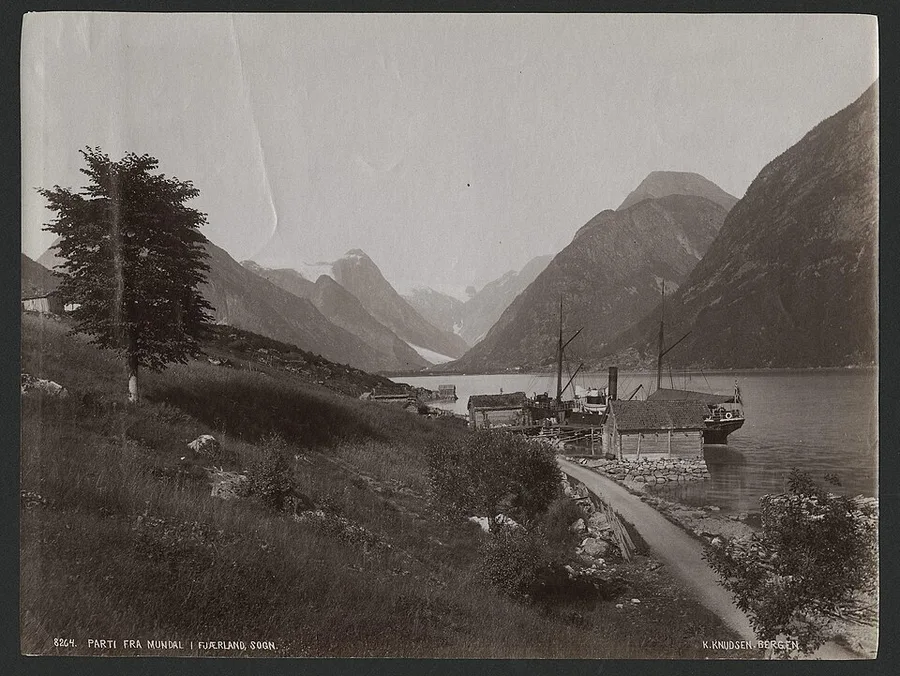Knud Knudsen's 1885 photograph of Mundal in Fjærland, Sogn — a fjord-arm village with its steamer at the pier, the glacier gleaming at the valley head.