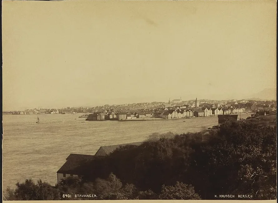 Knud Knudsen's photograph of Stavanger in the late 1880s–early 1890s — the low wooden town spread around its harbour, church towers on the skyline, decades before the oil age.
