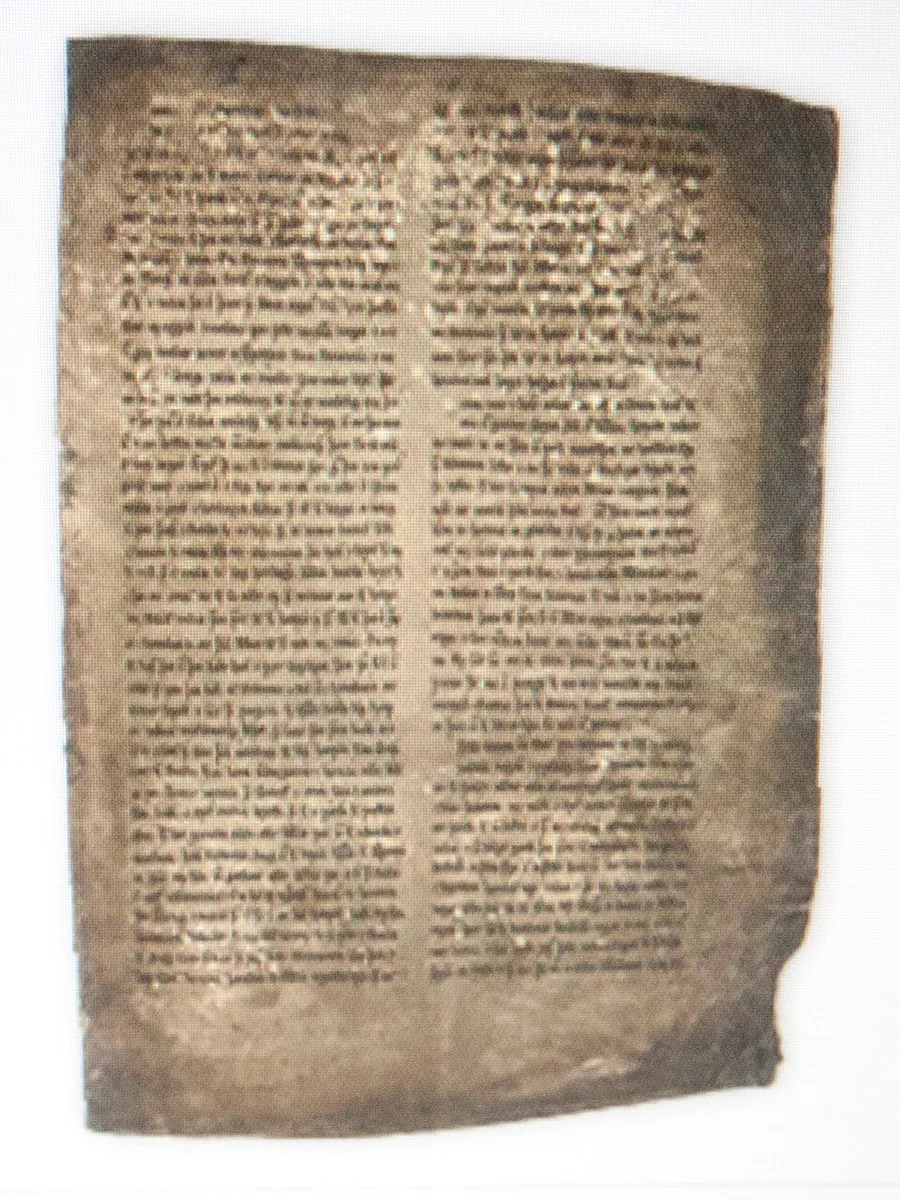 Photograph of an aged vellum manuscript leaf: dense two-column medieval script in brown ink, browned and worn at the edges.