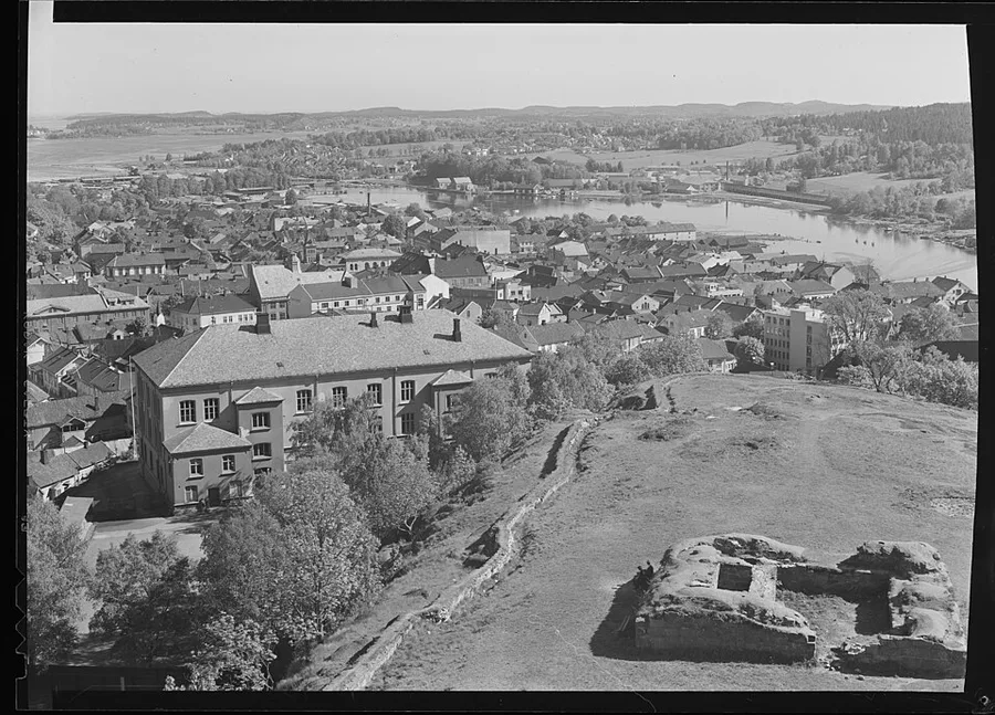 A mid-20th-century aerial photograph looking down from the Slottsfjellet fortress ruins over Tønsberg's rooftops to the river and fjord beyond.