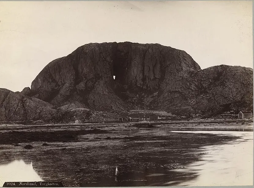Axel Lindahl's 1880s photograph of Torghatten — the pierced granite dome above the shore flats, the hole showing as a bright notch through the mountain's dark mass.