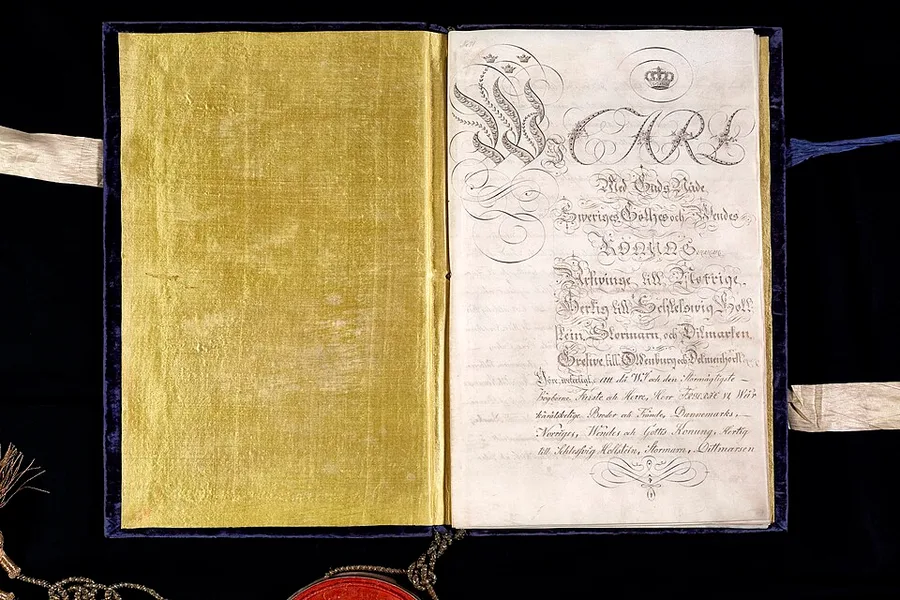 Photograph of the open, velvet-bound 1814 Treaty of Kiel document: a gold silk endpaper at left facing an ornately calligraphed vellum page beginning 'Carl... Sweriges Gothes och Wendes Konung,' with a wax seal and ribbons visible at the bottom.