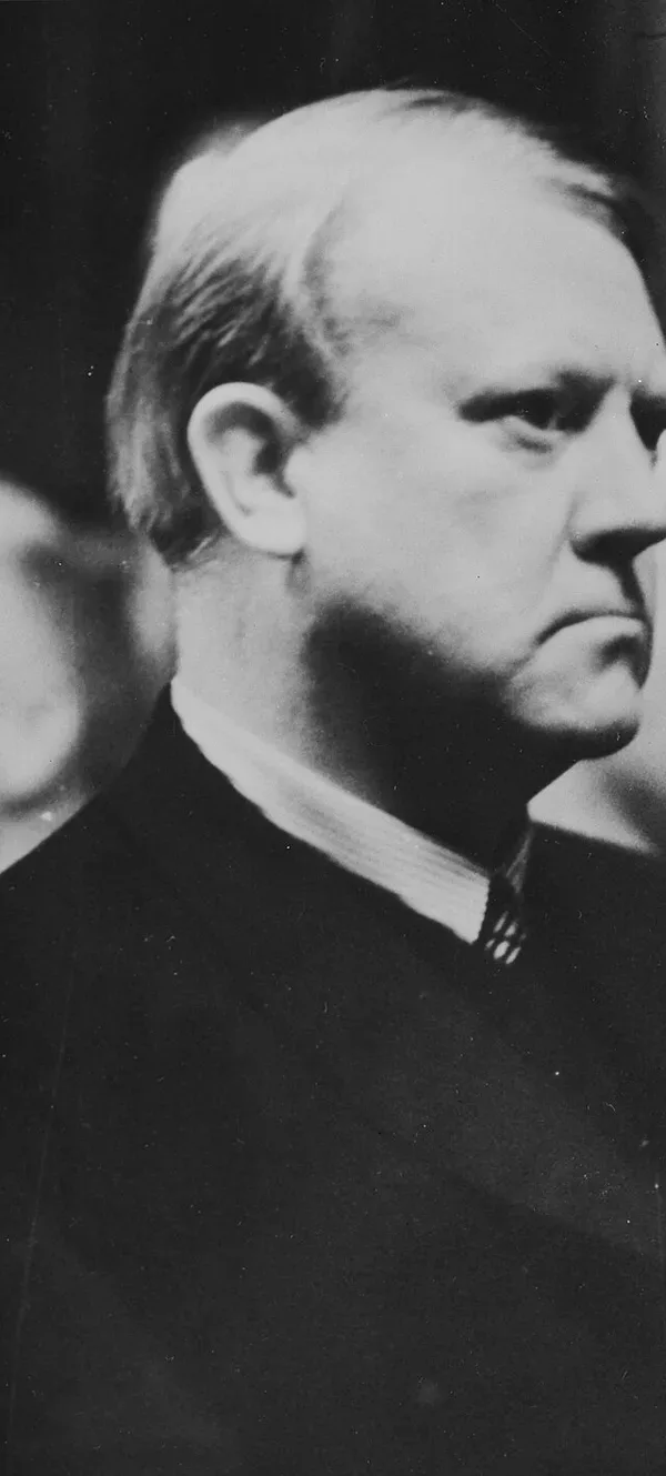 Black-and-white 1940 photograph, cropped to Vidkun Quisling's profile: balding, light-haired, in a dark coat and white collar, stern expression; a second man's face is faintly visible at lower left.