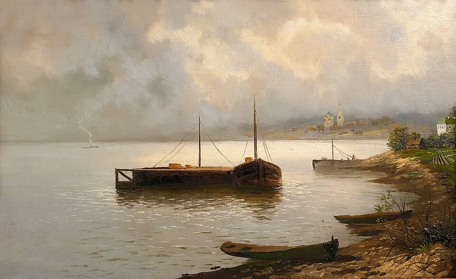 Isaac Levitan's 1889 river landscape: a large wooden barge and a smaller rowboat rest at anchor on the calm, hazy Volga under a luminous cloud-filled sky, with two beached rowboats and a low riverbank village with a church spire in the distance.